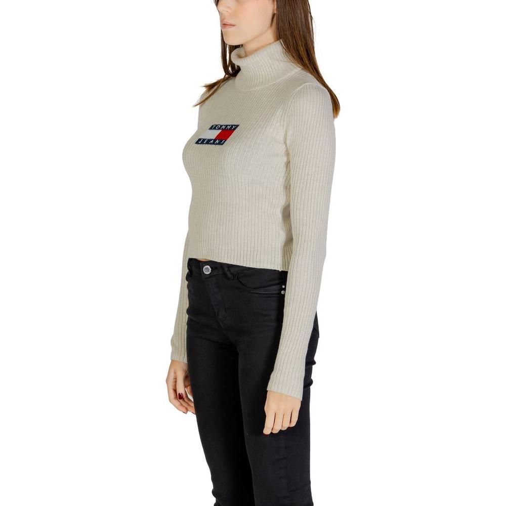 Woman wearing beige Tommy Hilfiger recycled polyester sweater, fall/winter collection, featuring logo, long sleeves, turtleneck.