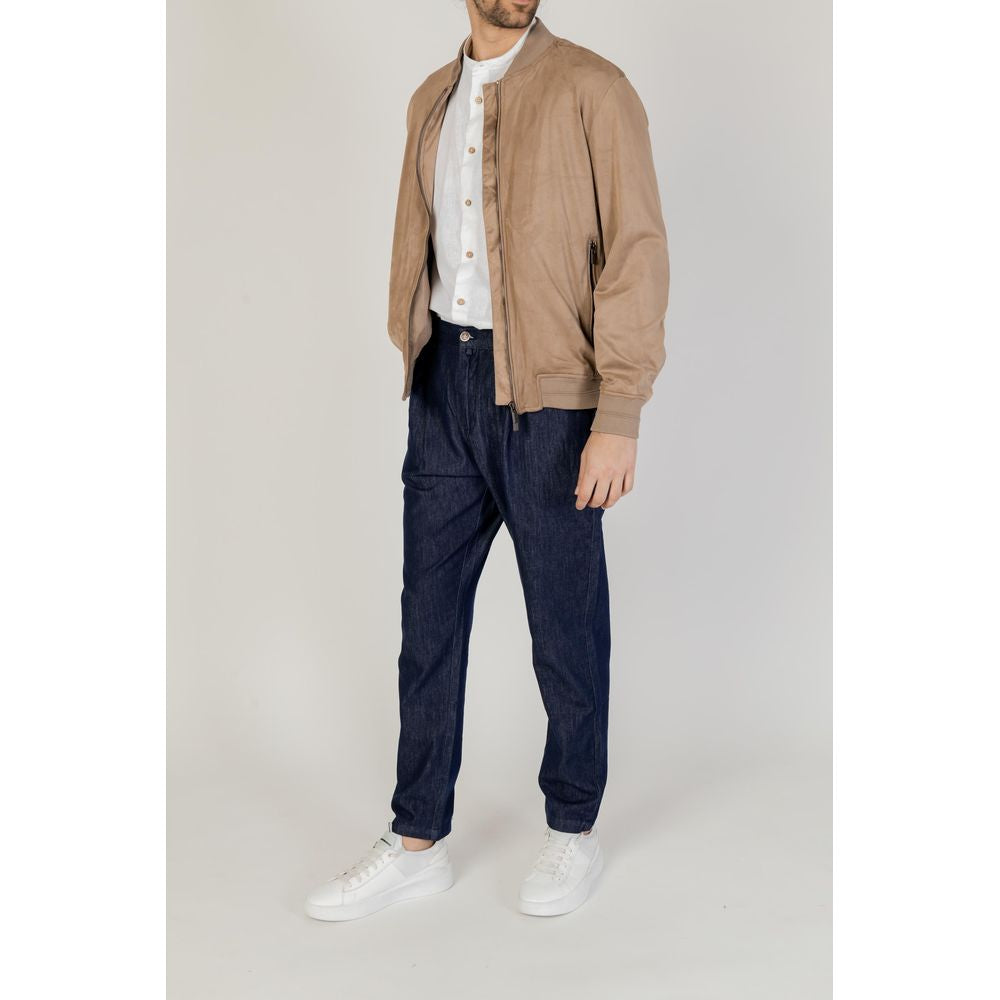 Man wearing a casual outfit with a tan jacket, white shirt, blue jeans, and white sneakers, standing against a neutral background.