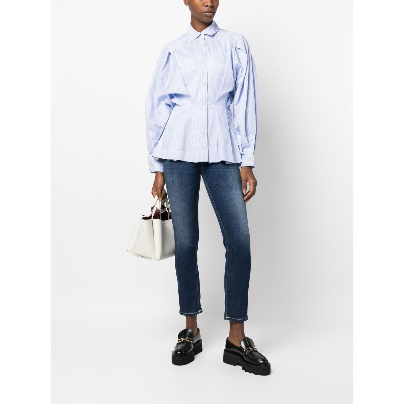 Model wearing a pastel blue cotton gathered-waist shirt by Palmer//Harding with jeans and black loafers, holding a white handbag.