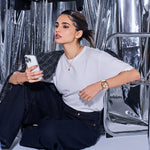 Person wearing CASIO G-SHOCK WATCHES Mod. GM-S2110PG-4AER, holding smartphone, sitting against metallic background.