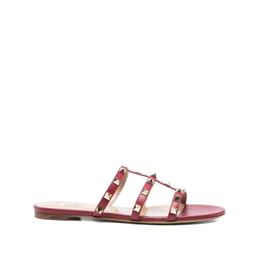 Valentino Garavani Rockstud three-strap sandals in red calf leather with flat sole, open toe, and signature studded embellishments.